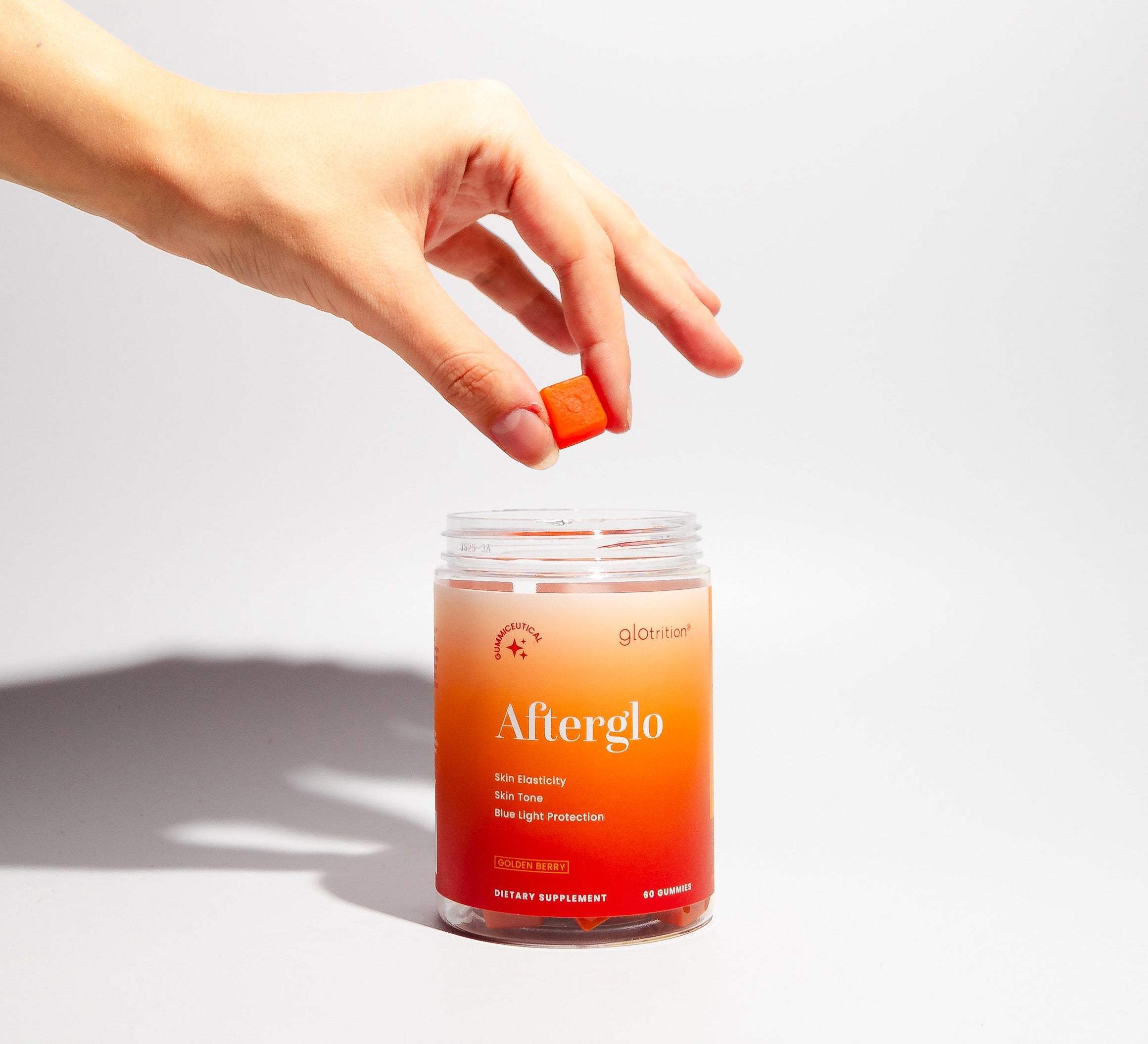 Hand picking a Glotrition Afterglo gummy from open jar – golden berry gummiceutical for skin elasticity, tone, and blue-light protection.